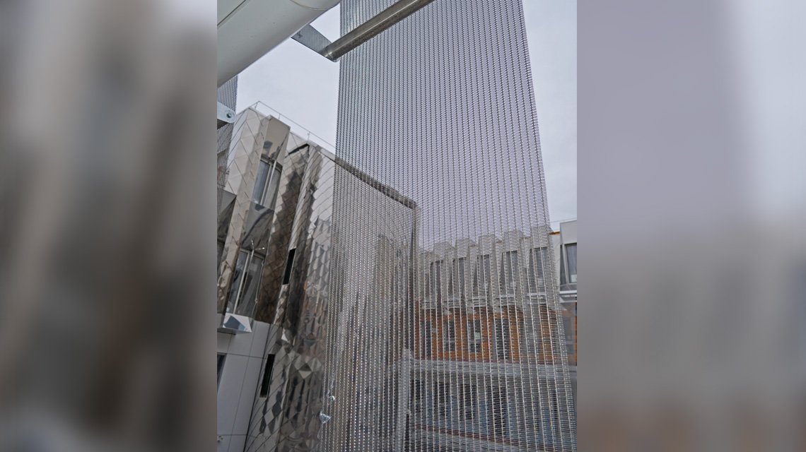 Malha metálica aramada SATURN, fabricada à medida em aço inoxidável 316L e instalada em tiras e painéis em ziguezague na fachada do edifício residencial. A malha metálica combina estética e funcionalidade como quebra-sol. - <p>Malha metálica aramada SATURN, fabricada à medida em aço inoxidável 316L e instalada em tiras e painéis em ziguezague na fachada do edifício residencial. A malha metálica combina estética e funcionalidade como quebra-sol.</p>